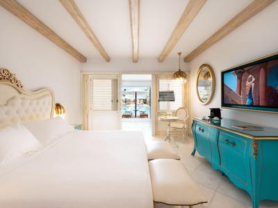 Světelná ložnice s bílými stěnami, dřevěnými trámy a výhledem na terasu a moře.