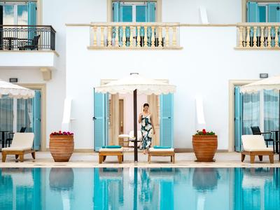 Žena stojí před bílou budovou s modrými okenicemi vedle bazénu.