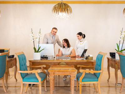 Drei Personen am Empfang eines Hotels mit blau gepolsterten Stühlen und Holztheke.