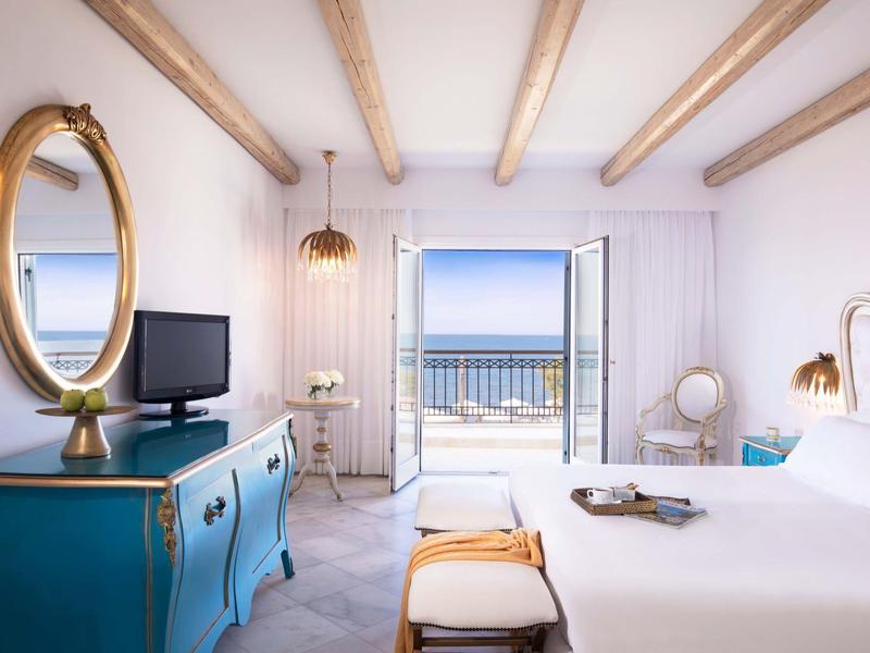 Camera d'hotel luminosa con vista sul mare, pareti bianche e mobili blu.