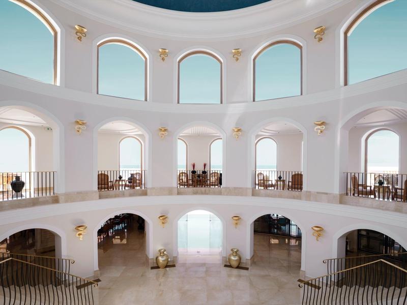 Interno luminoso su due piani con pareti bianche, archi e soffitto a cupola blu.