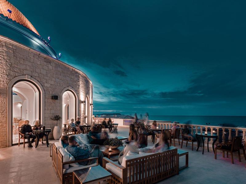 Terrazza dell'hotel al tramonto con posti a sedere e vista mare sotto un cielo scuro.