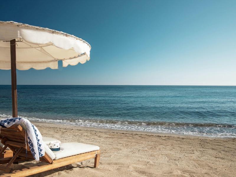 Sdraio con ombrellone su una spiaggia di sabbia tranquilla con vista sul mare blu sotto un cielo sereno.