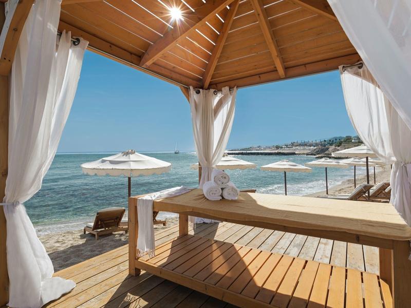 Tavolo da massaggio rilassante in una capanna sulla spiaggia con vista sull'oceano e ombrelloni.