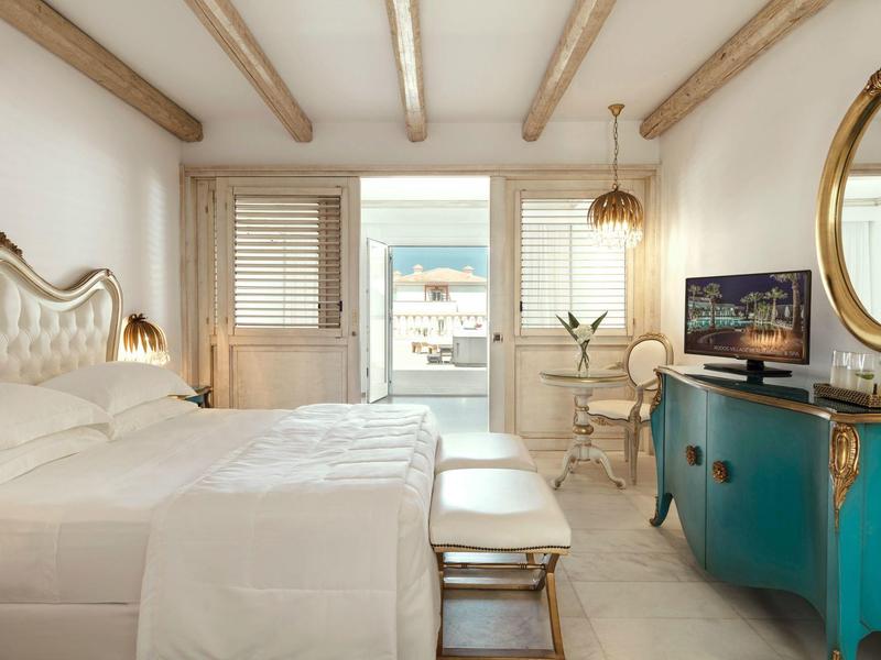 Camera d'hotel luminosa con letto matrimoniale, credenza turchese e balcone con vista mare.