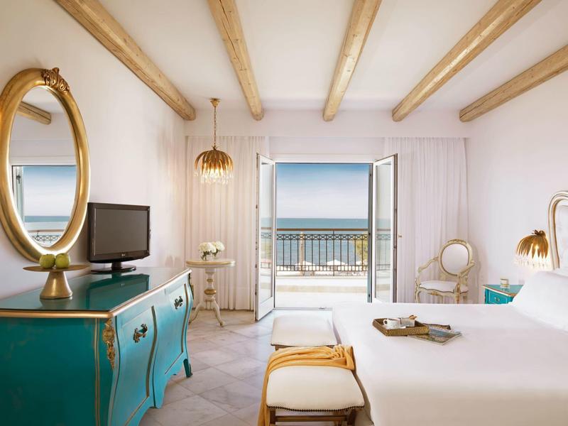 Camera d'albergo luminosa con vista mare attraverso porte aperte e interno elegante.