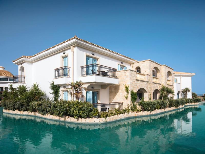 Edificio alberghiero moderno con balconi su un canale d'acqua blu chiaro sotto un cielo sereno.