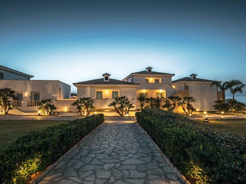 Grande edificio dell'hotel illuminato al crepuscolo con giardino anteriore curato e sentiero.