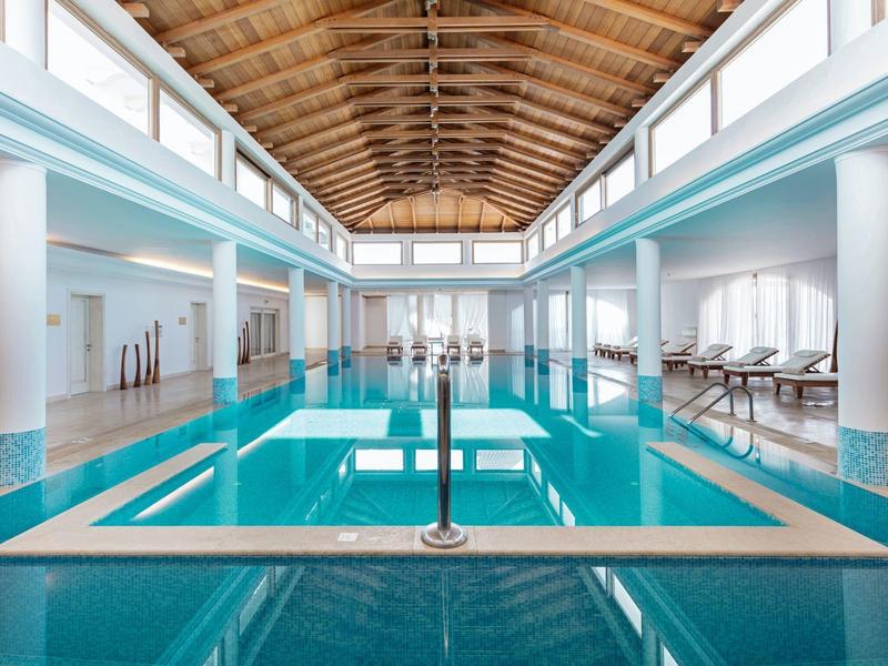 Piscina interna luminosa con soffitto in legno e lettini ai lati.
