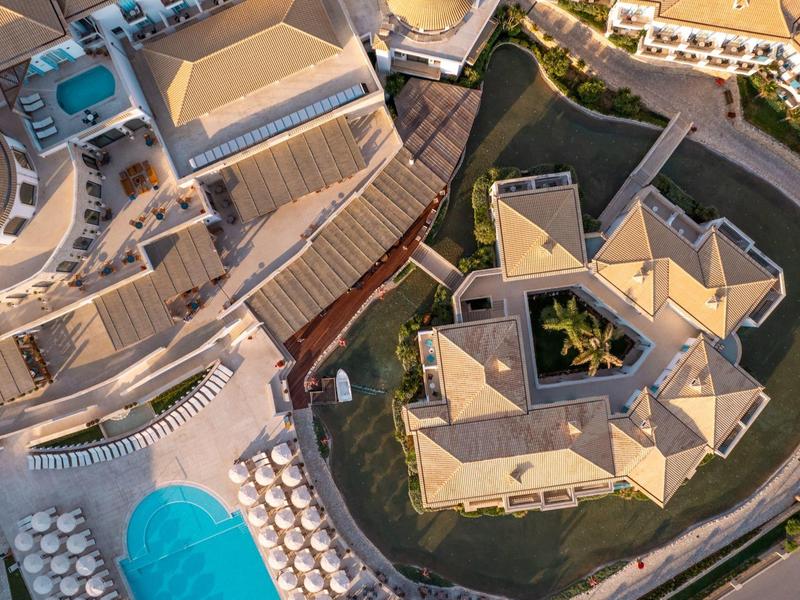 Vista aerea di un hotel con piscina blu, lettini e una struttura edilizia dalla forma insolita.