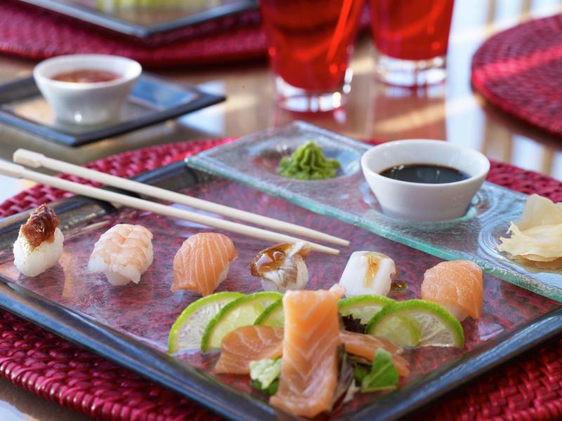 Un vassoio con vari tipi di sushi, fette di lime e salsa di soia su un tovaglietta rossa.