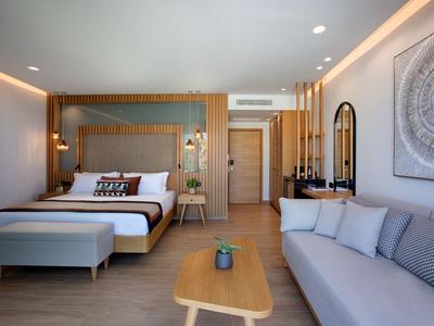 Moderner Wohnbereich mit großem Bett, grauer Couch, Holzmöbeln und dezentem Wandbild.