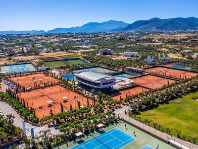 Luftaufnahme eines großen Tenniszentrums mit vielen Sand- und Hartplätzen, umgeben von Bergen.