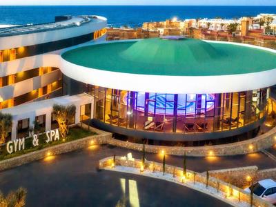 Modernes Gym & Spa mit rundem, beleuchtetem Eingangsbereich und umliegender Hotelanlage bei Abendlicht.