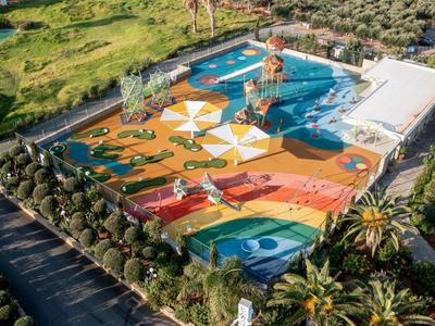Bunter, großer Kinderspielplatz mit Hüpfburg, Rutschen und Klettergerüsten, umgeben von Büschen und Bäumen.