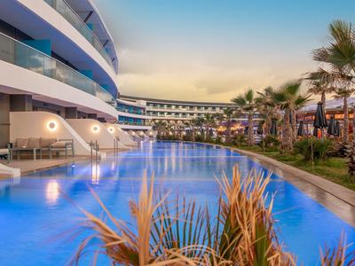 Moderner Hotelkomplex mit großem Pool und Palmen bei Sonnenuntergang.