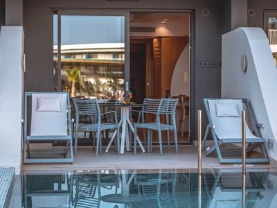 Moderner Außenbereich mit Pool, Stühlen und Tisch vor einer Hotelterrasse bei Sonnenuntergang.