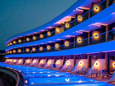 Beleuchtetes Hotel mit Balkon und Pool bei Nacht