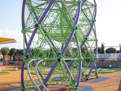 Grünes und lila Klettergerüst mit Seilnetz auf buntem Spielplatz bei Tageslicht.
