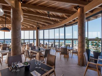 Hell eingerichtetes Restaurant mit großen Fenstern, Holzmöbeln und rustikalen Säulen aus Holz.