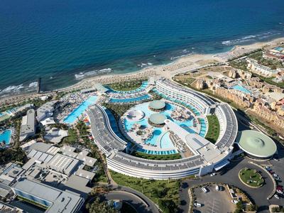 Großes halbmondförmiges Hotel mit mehreren Pools am Küstenstrand und angrenzenden Gebäuden.