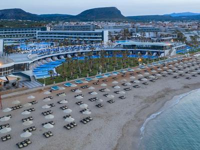 Strand mit geordneten Liegestühlen, großem Resort mit Pools und Hügeln im Hintergrund bei Sonnenuntergang.