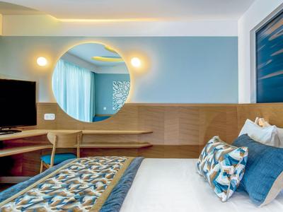 Modernes Hotelzimmer mit großem Bett, Rundspiegel und Holzvertäfelung an der Wand.