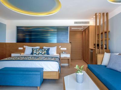 Modern eingerichtetes Hotelzimmer mit großem Bett, Sofa und dekorativem Deckenlicht.