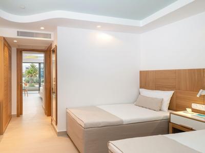 Klares Hotelzimmer mit zwei Einzelbetten und Holzmöbeln, offener Tür mit Blick nach draußen.