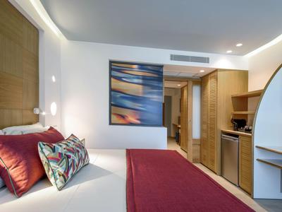 Modernes Hotelzimmer mit Doppelbett, roten Akzentkissen und abstraktem Kunstwerk an der Wand.