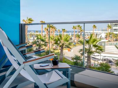 Balkon mit weißen Stühlen und Tisch, Blick auf Palmen und Meer in einem Hotel.