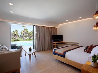 Modernes Hotelzimmer mit Doppelbett, Sofa, TV und Blick auf den Pool durch Schiebetür.