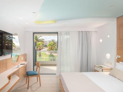 Helles, modernes Schlafzimmer mit Doppelbett, Schreibtisch, Stuhl und großem Fenster mit Blick ins Grüne.