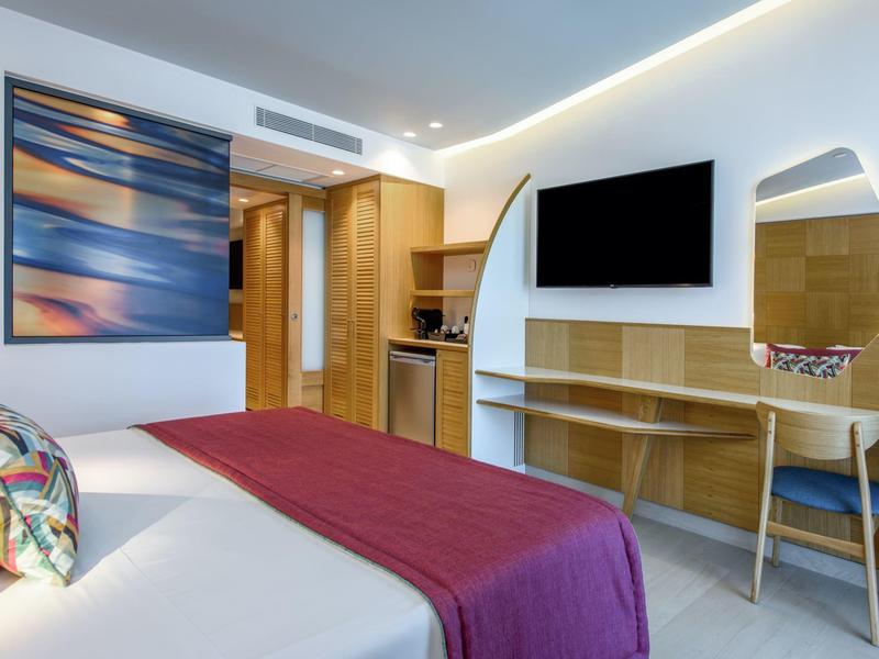 Habitación de hotel con cama doble, escritorio, televisor y decoración moderna en tonos cálidos.