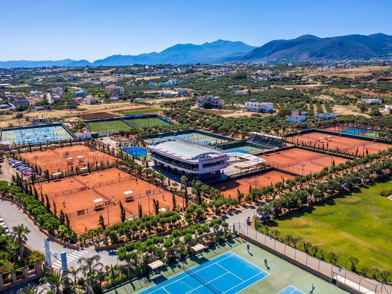 Gran complejo de tenis con muchas canchas de tierra y cemento, rodeado de montañas y naturaleza.