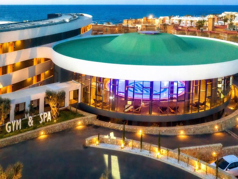 Complejo hotelero moderno con edificio circular iluminado y piscina al atardecer.