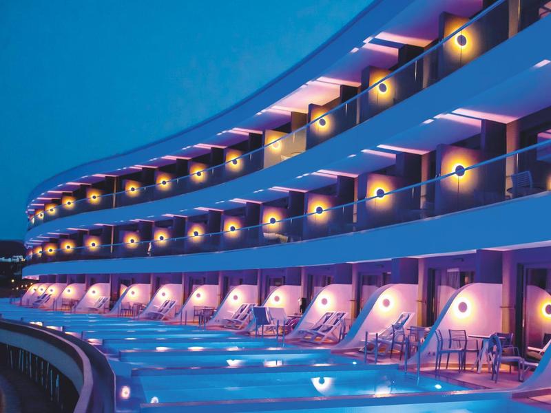 Edificio de hotel moderno con luces violetas y piscina iluminada al anochecer