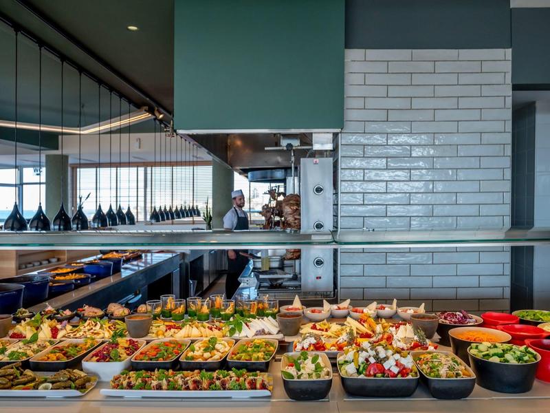 Buffet con variedad de ensaladas y platos en restaurante moderno con grandes ventanales.