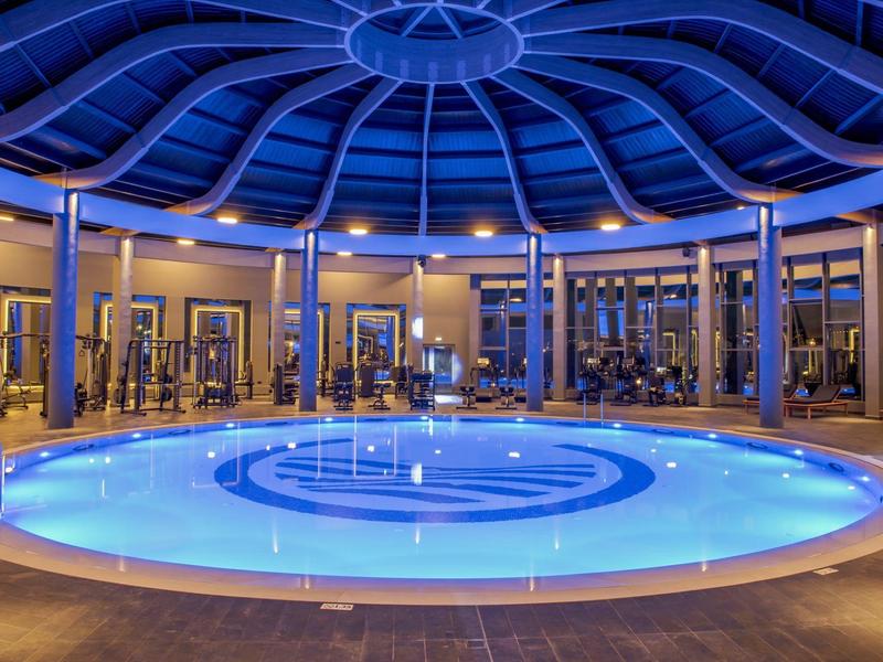 Piscina cubierta redonda climatizada con iluminación azul y paredes de vidrio en un hotel.