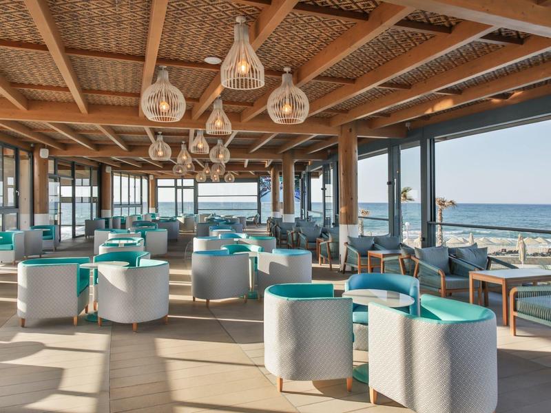 Restaurante de playa moderno con sillas blancas y detalles turquesa con vista al mar.