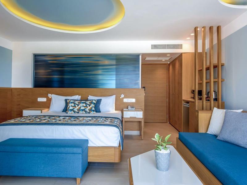 Habitación de hotel moderna con cama doble, banco azul, sofá y decoración contemporánea.