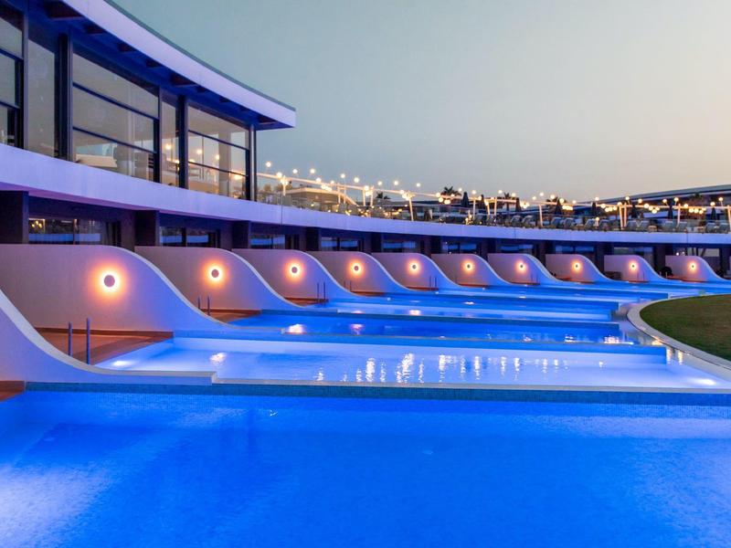 Piscina moderna de hotel al anochecer con iluminación y área de descanso