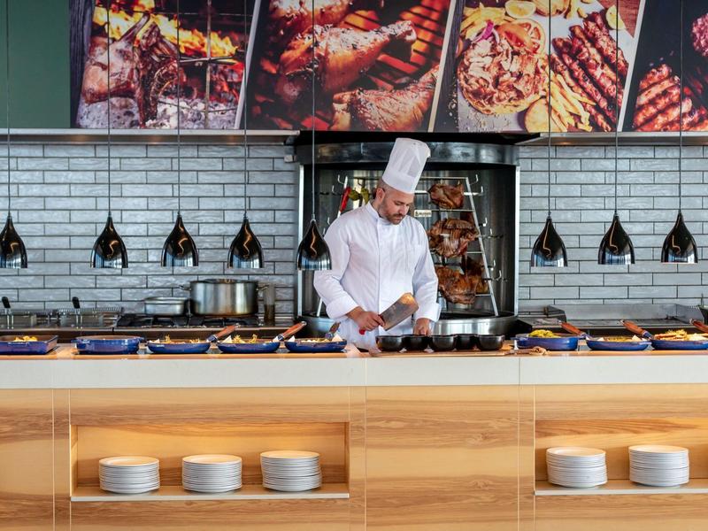 Un chef con uniforme blanco prepara comida en el buffet de un restaurante moderno.
