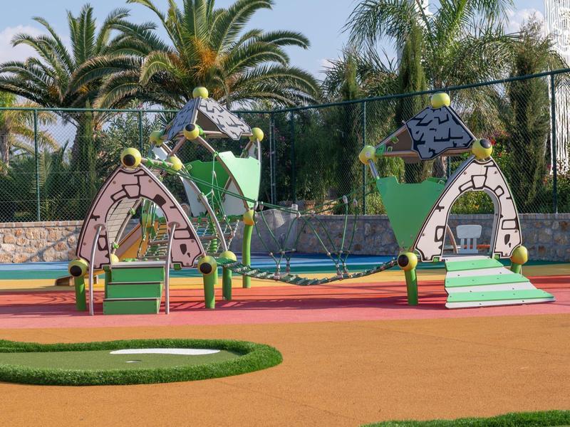 Área de juegos para niños al aire libre con estructuras de plástico y árboles de fondo.