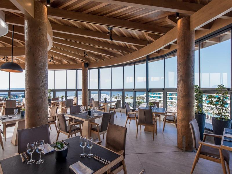 Un restaurante moderno con vigas de madera y grandes ventanas con vista al mar.