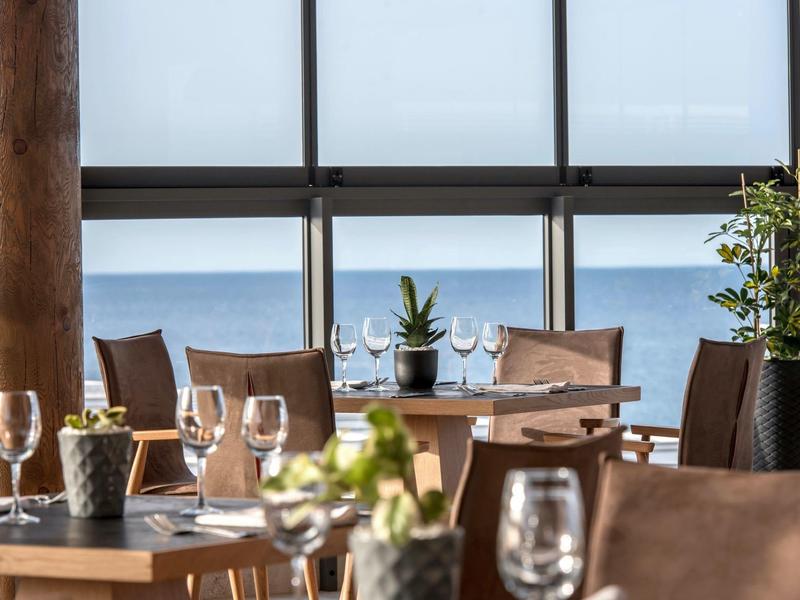 Restaurante del hotel con mesas de madera, sillas y vista al mar a través de grandes ventanas.