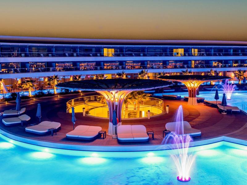 Hotel moderno con piscina iluminada y cómodas tumbonas al atardecer.
