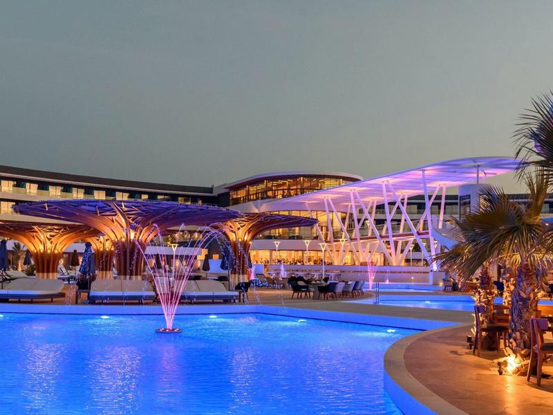 Hotel iluminado con piscina azul y elementos arquitectónicos modernos al atardecer.