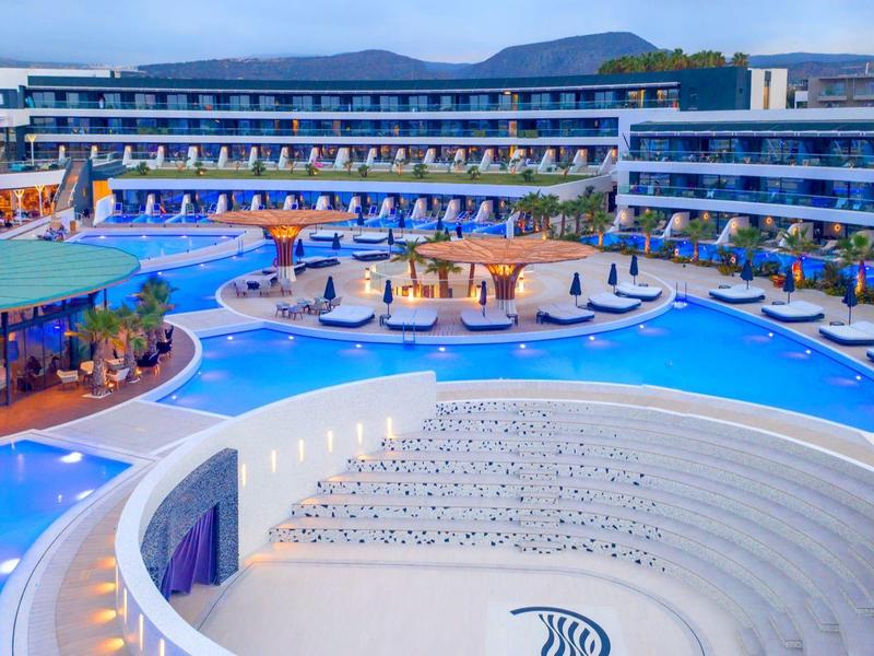 Complejo hotelero moderno con varias plantas, gran piscina y restaurante al aire libre bajo cielo despejado.