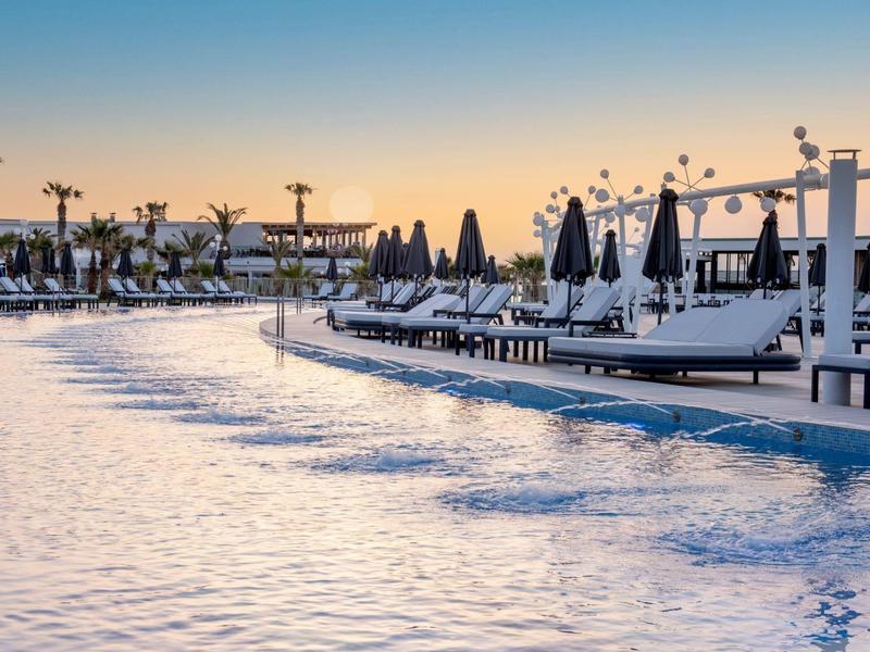 Gran piscina del hotel con tumbonas y sombrillas al atardecer en entorno tropical.